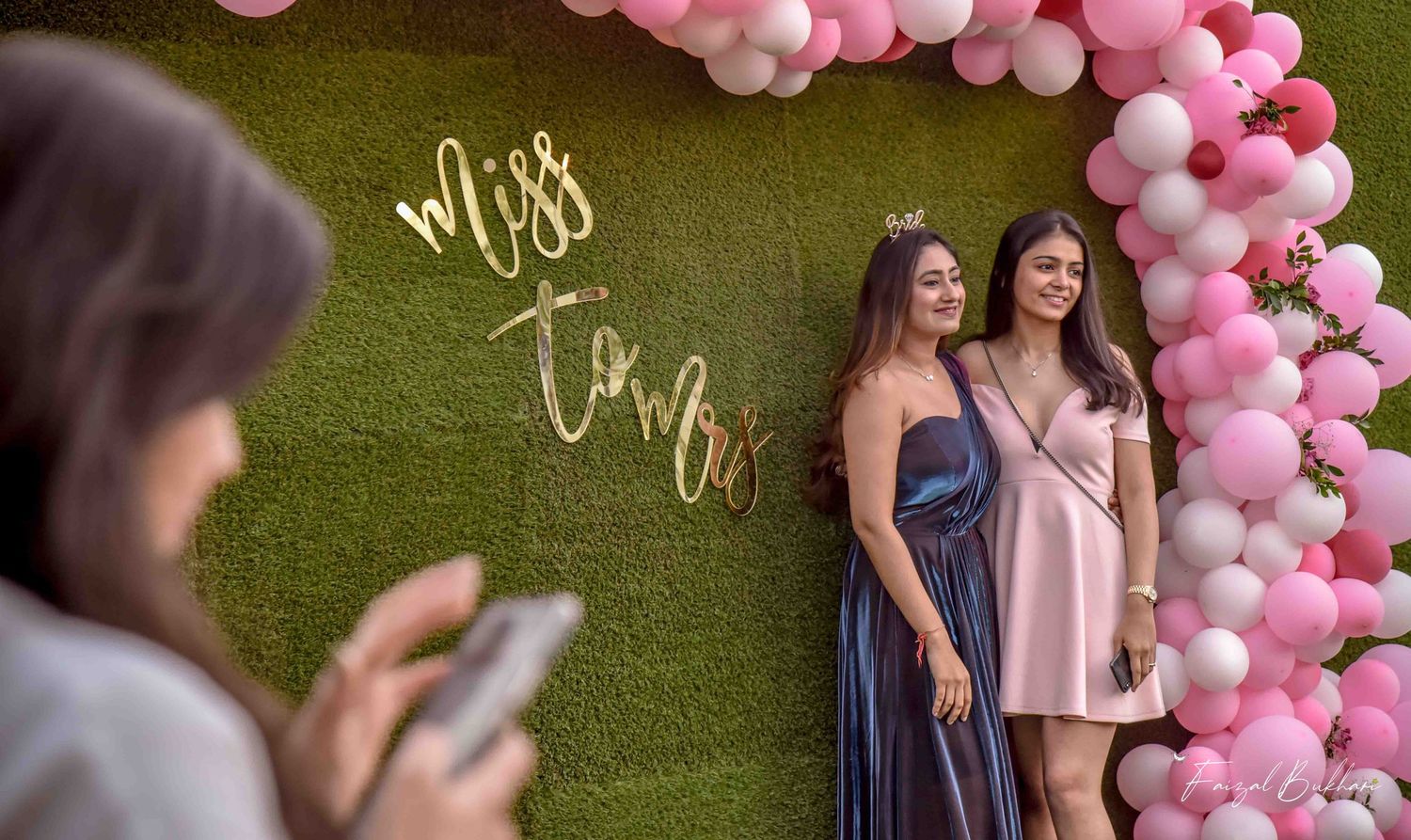 Two women pose in front of a Miss to Mrs balloon arch backdrop at a bridal shower celebration.
