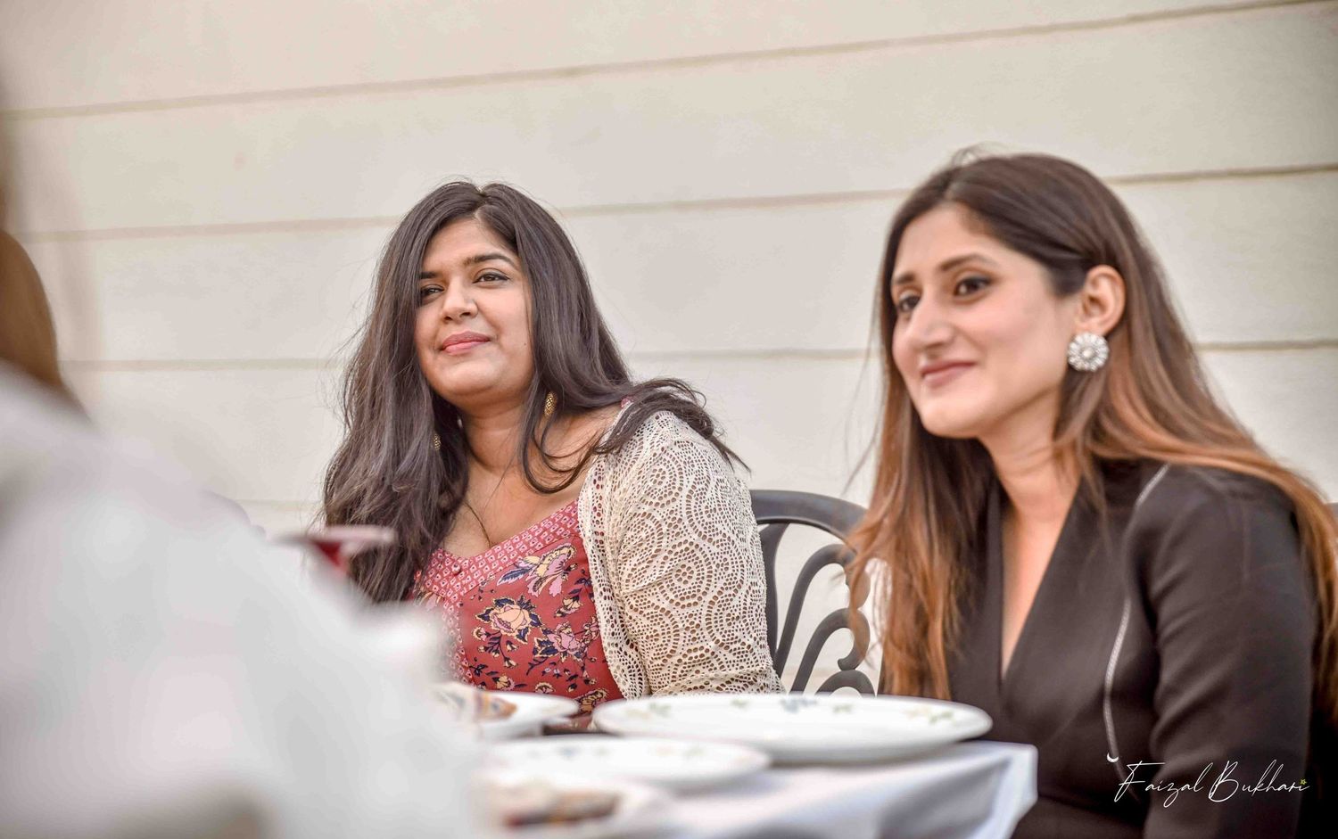 Two elegantly dressed women smiling at outdoor bridal shower celebration table.