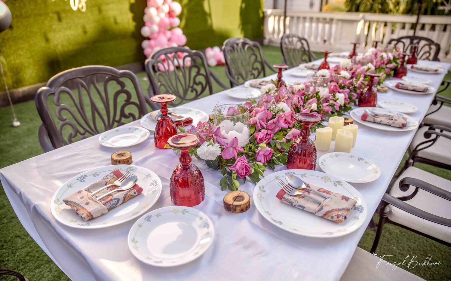 Beautifully set outdoor bridal shower table with pink floral runner, red goblets, and white plates.