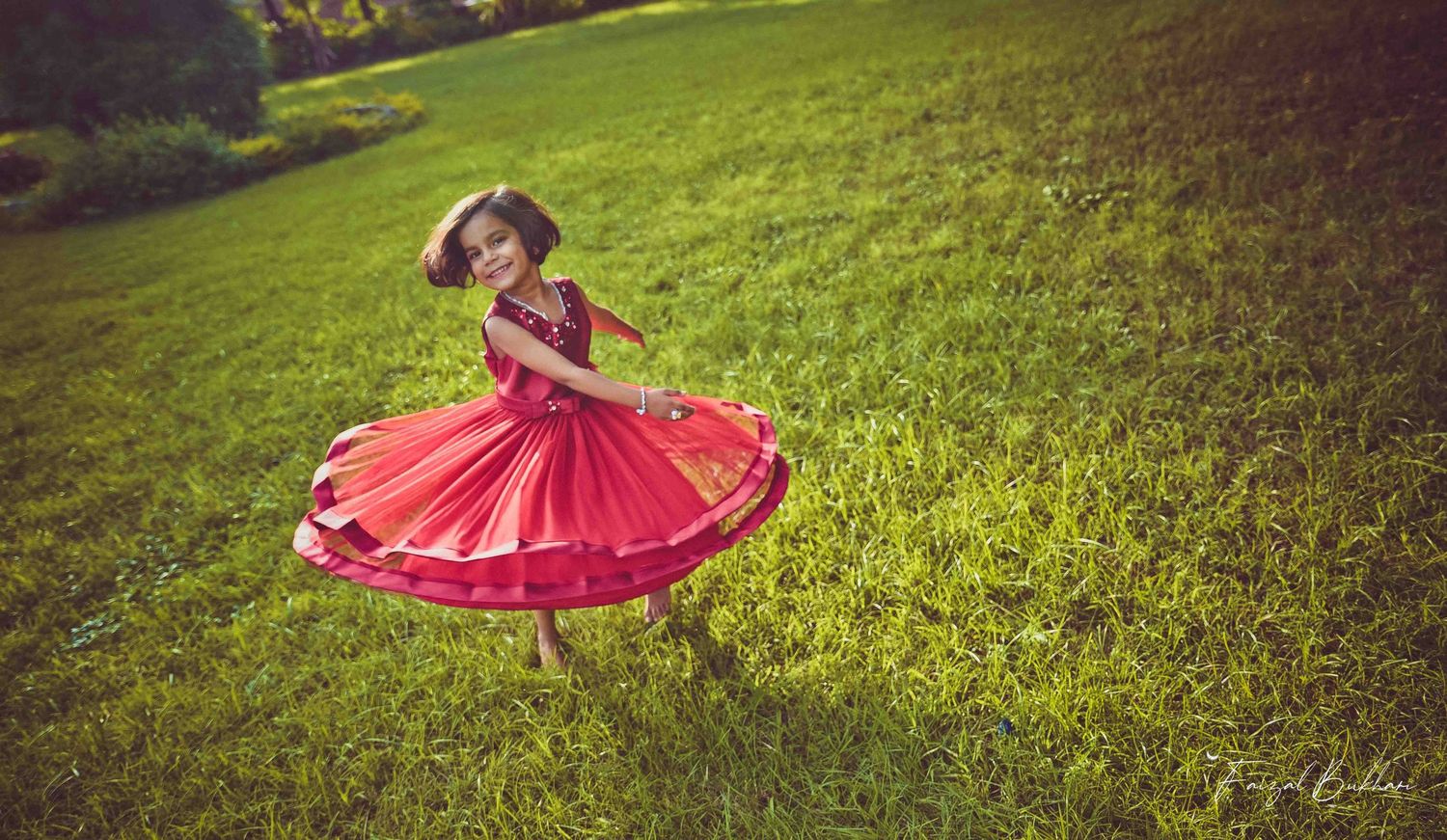 A young girl in a vibrant red dress twirls joyfully on a lush green lawn in golden sunlight.