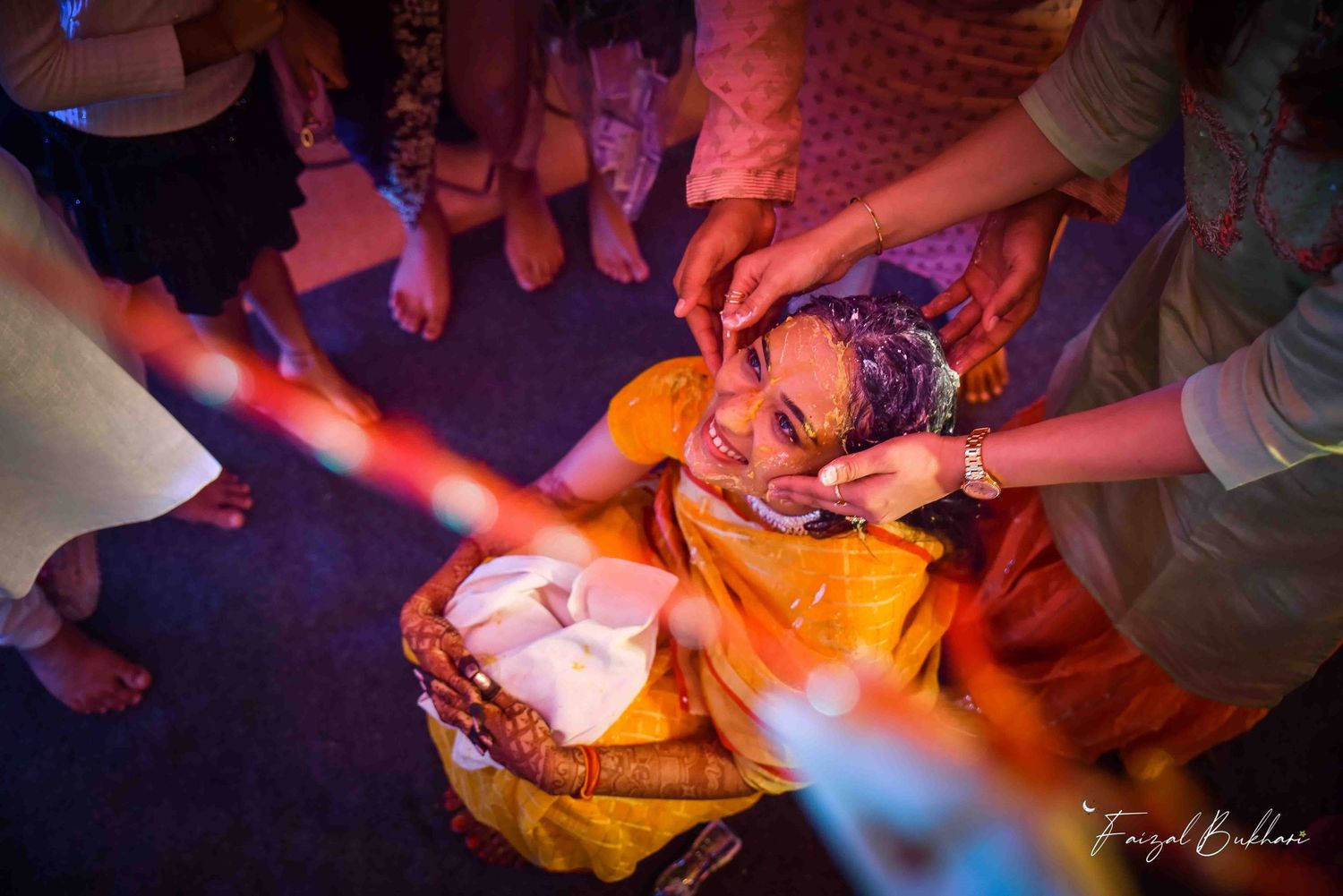 Overhead view of Indian bride in yellow outfit during traditional haldi ceremony with family members.