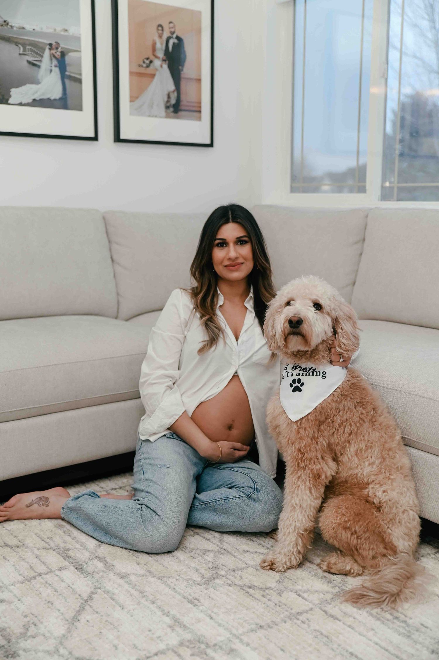 Pregnant woman in white shirt sitting on floor with golden doodle dog wearing a big brother bandana.