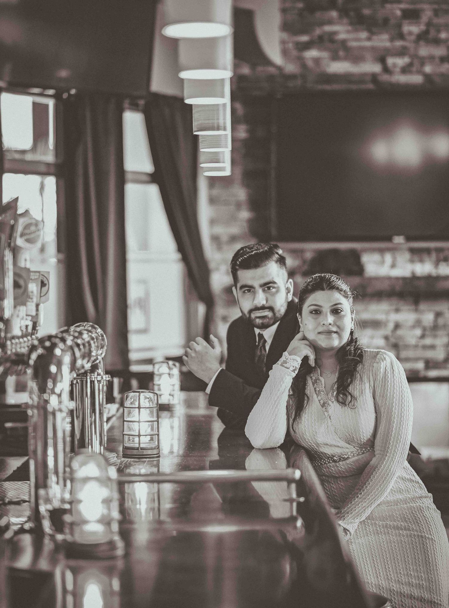 Couple poses at a bar counter in sepia-toned pre-wedding photo shoot inside a vintage restaurant setting.