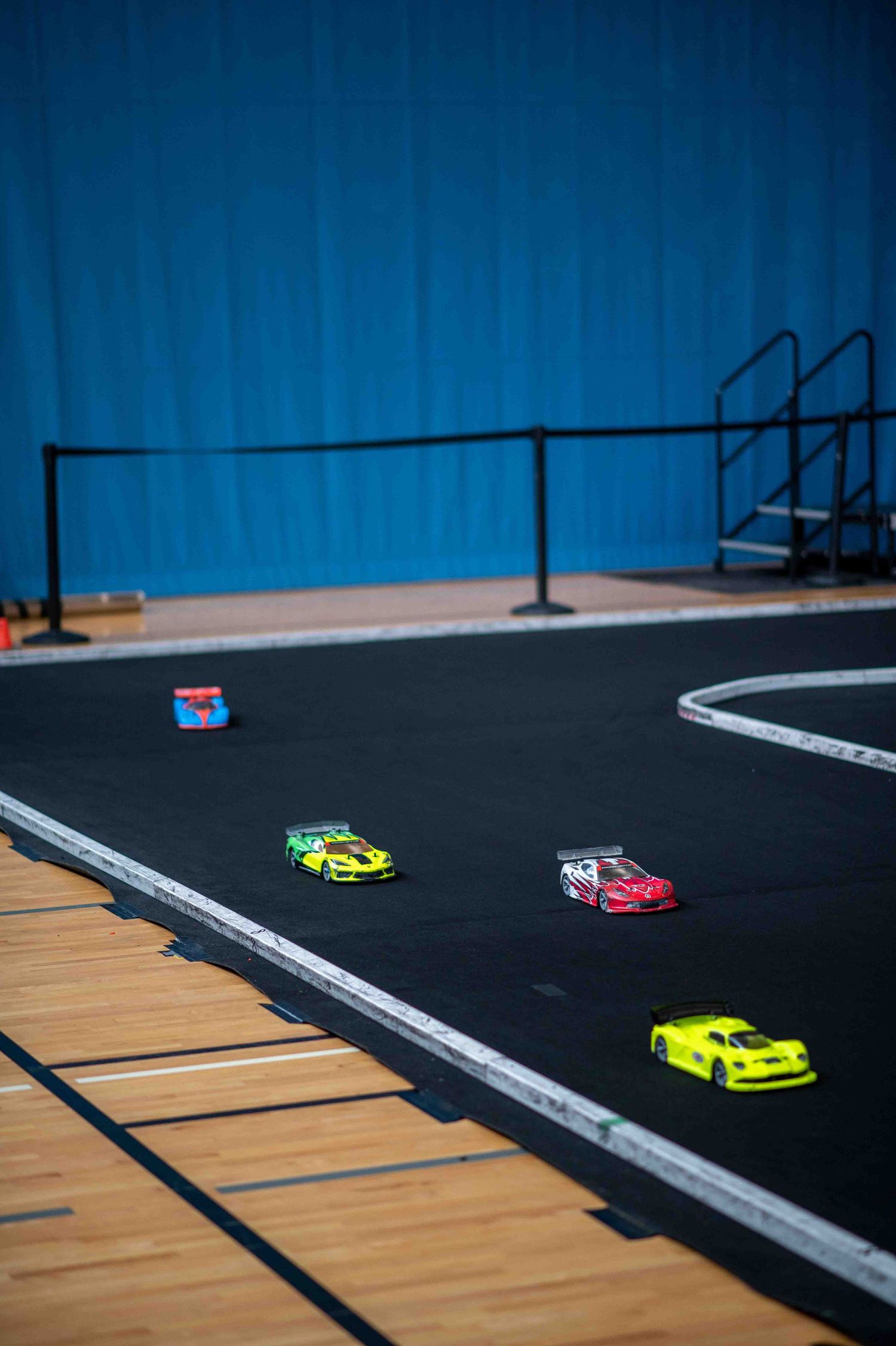 Multiple colorful RC cars racing on a black indoor carpet track during a competition.