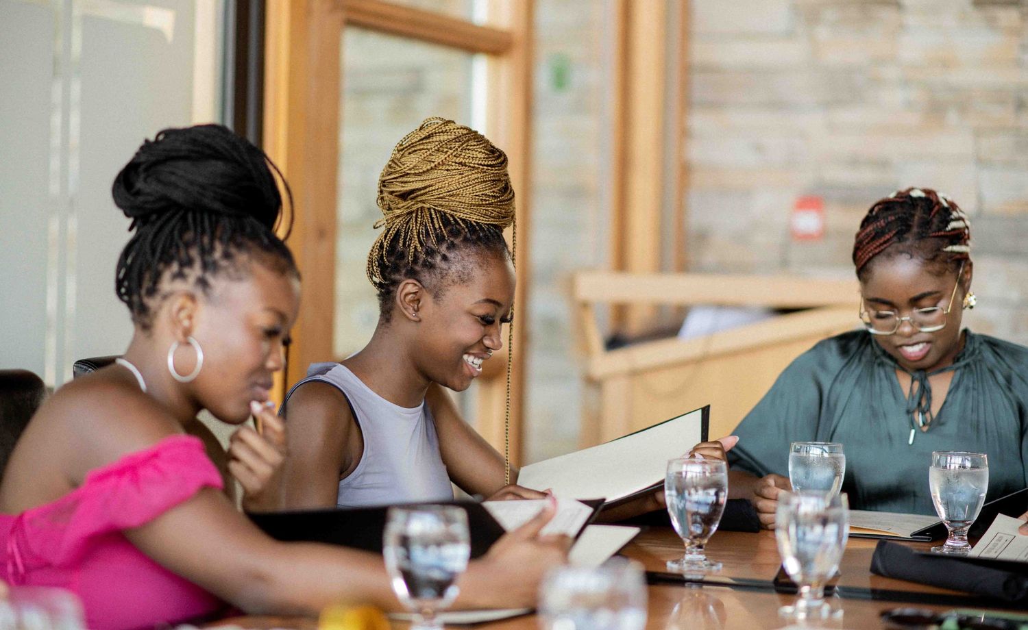 Three women laughing and reviewing menus together at a restaurant dining table with water glasses.