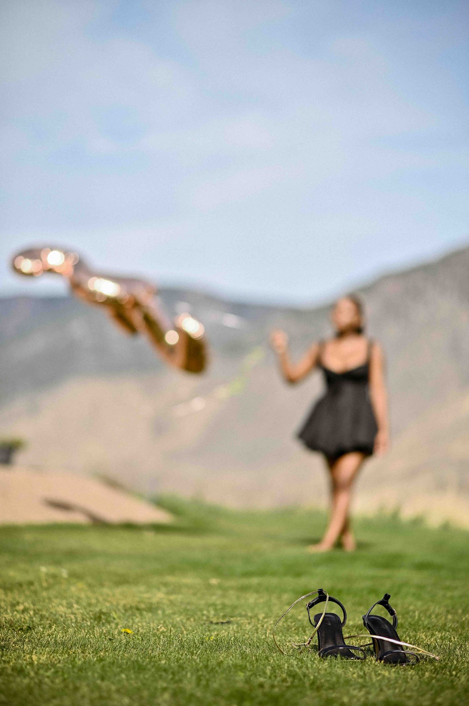 Woman in black dress releasing gold balloons on green golf course with mountain backdrop.
