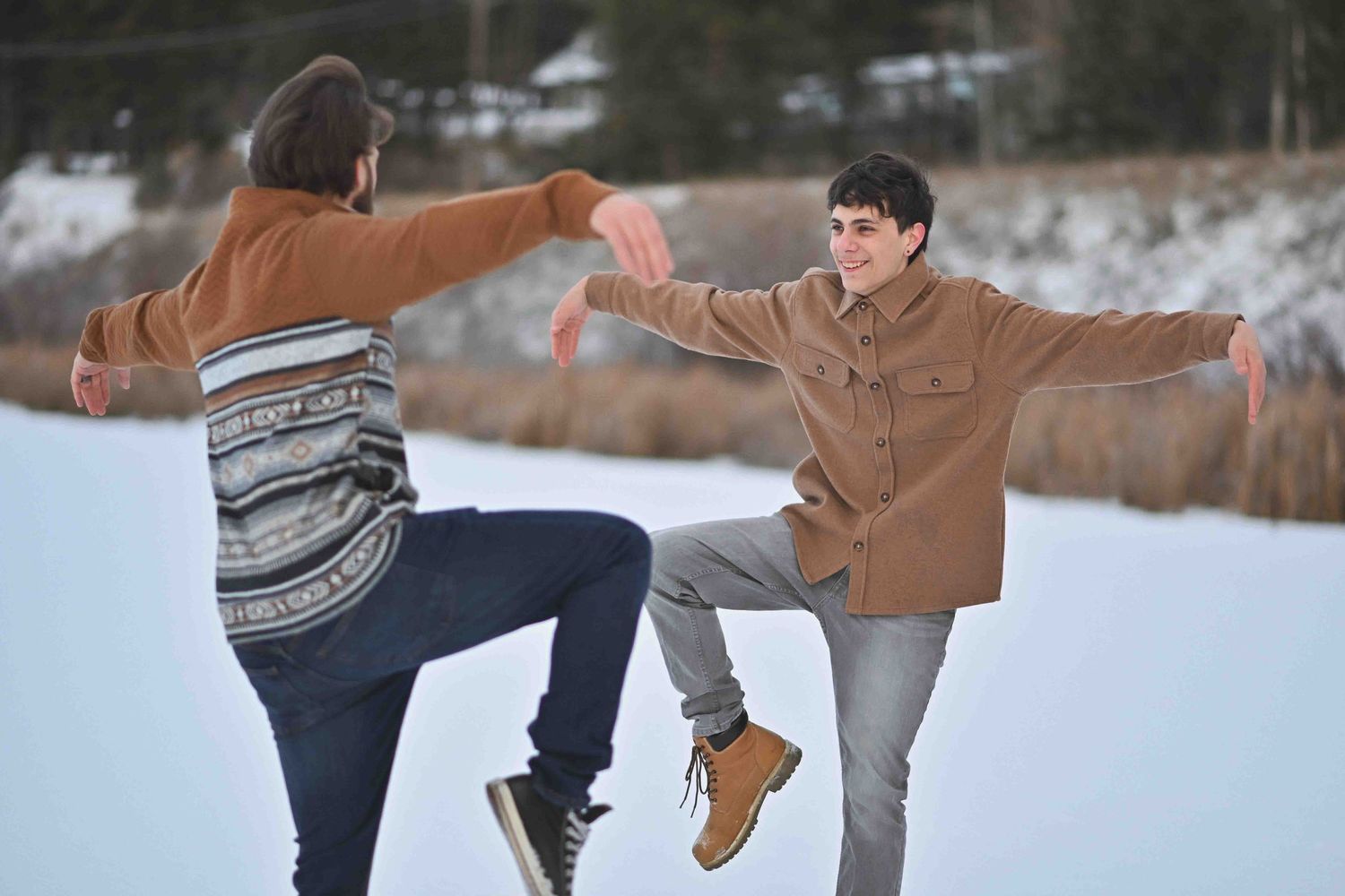 Two young men playfully balance on a snowy winter landscape, arms outstretched in a fun outdoor photo session.
