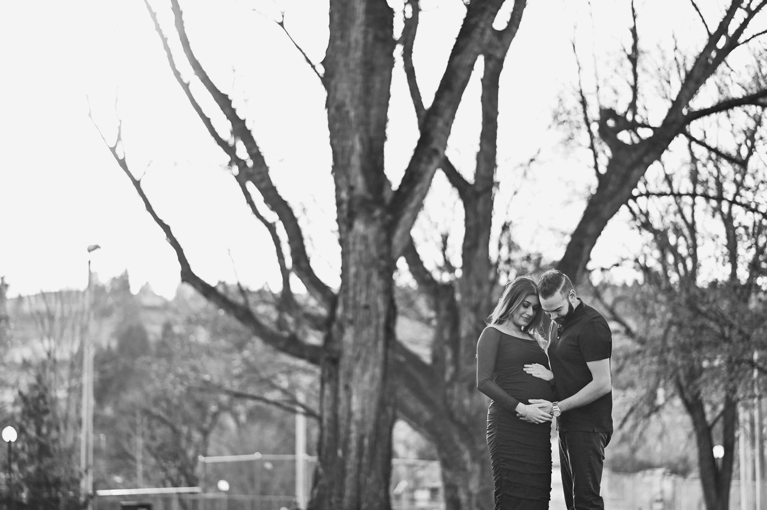 Black and white photo of couple embracing tenderly during outdoor maternity session.