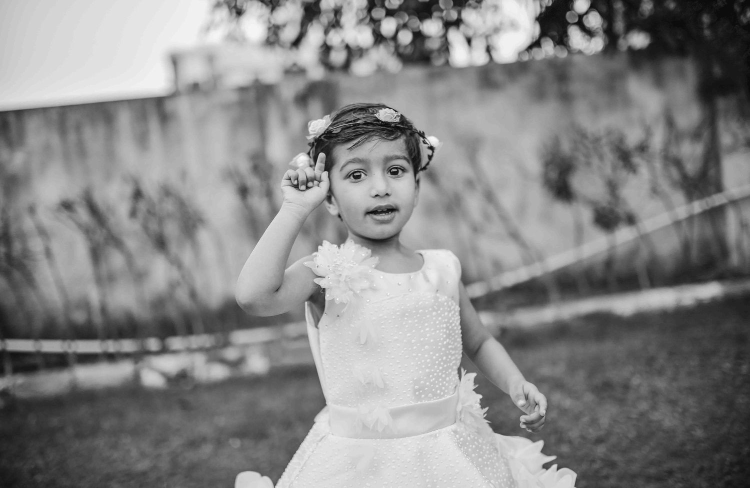 Black and white photo of a young girl in white dress and floral headband playing outdoors.