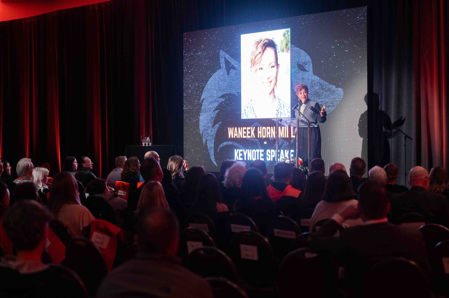 Keynote speaker Waneek Horn-Miller presenting on stage before a large seated audience at a formal event.