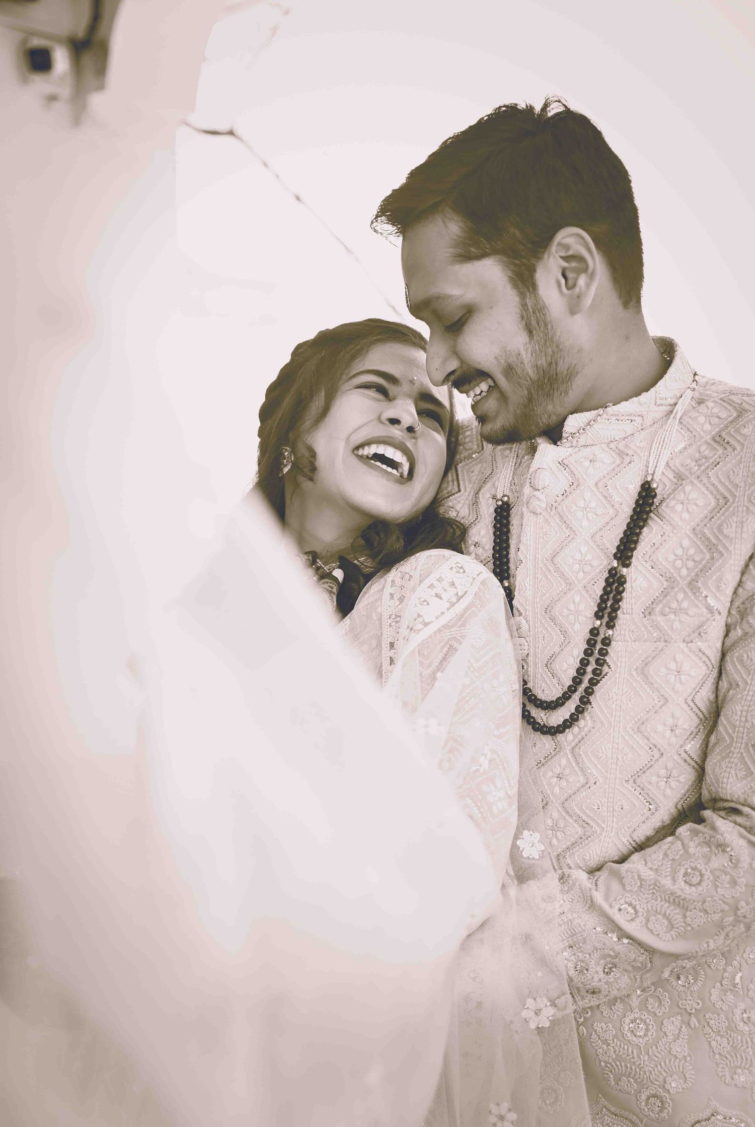 A joyful Indian bride and groom sharing a romantic laugh during their traditional wedding ceremony.