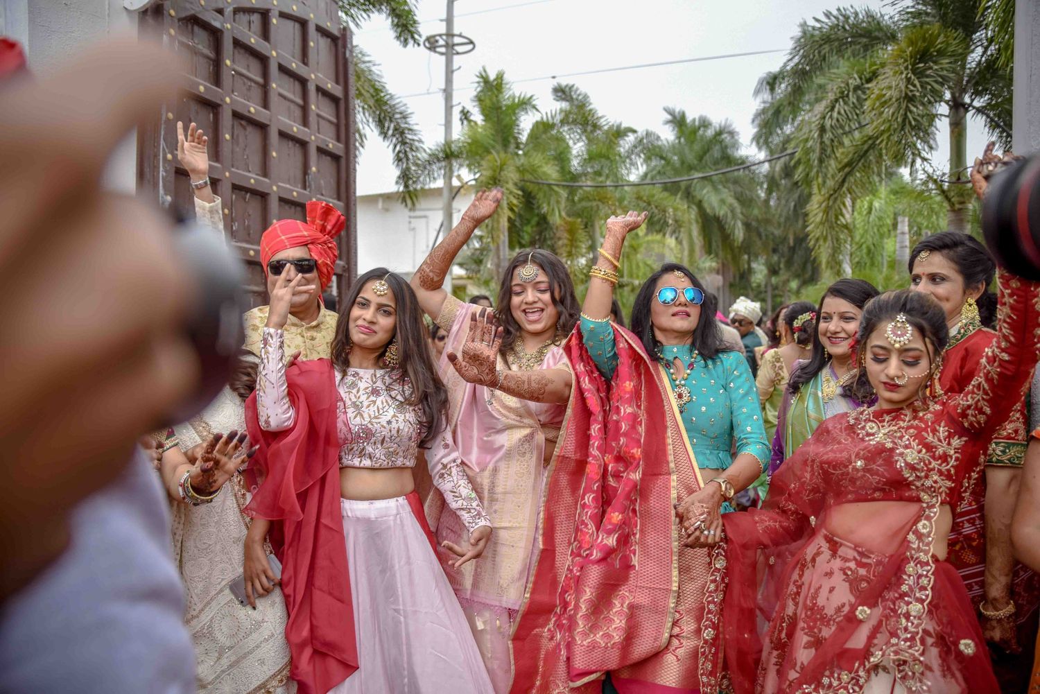 Colorful Indian wedding baraat procession with bride and guests dancing joyfully in traditional red and pink lehengas.