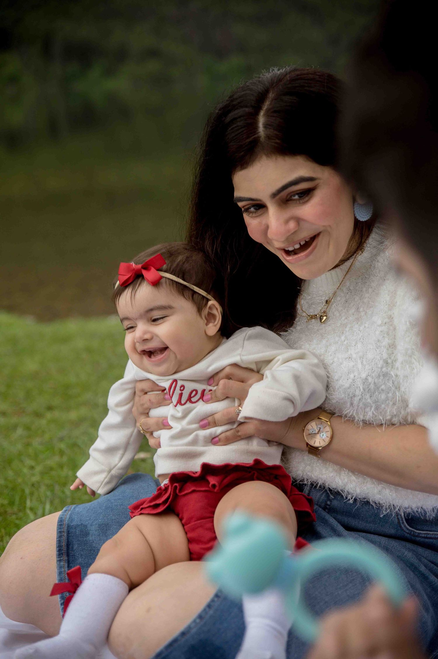 Mother laughing joyfully while holding her giggling baby girl with a red bow headband.