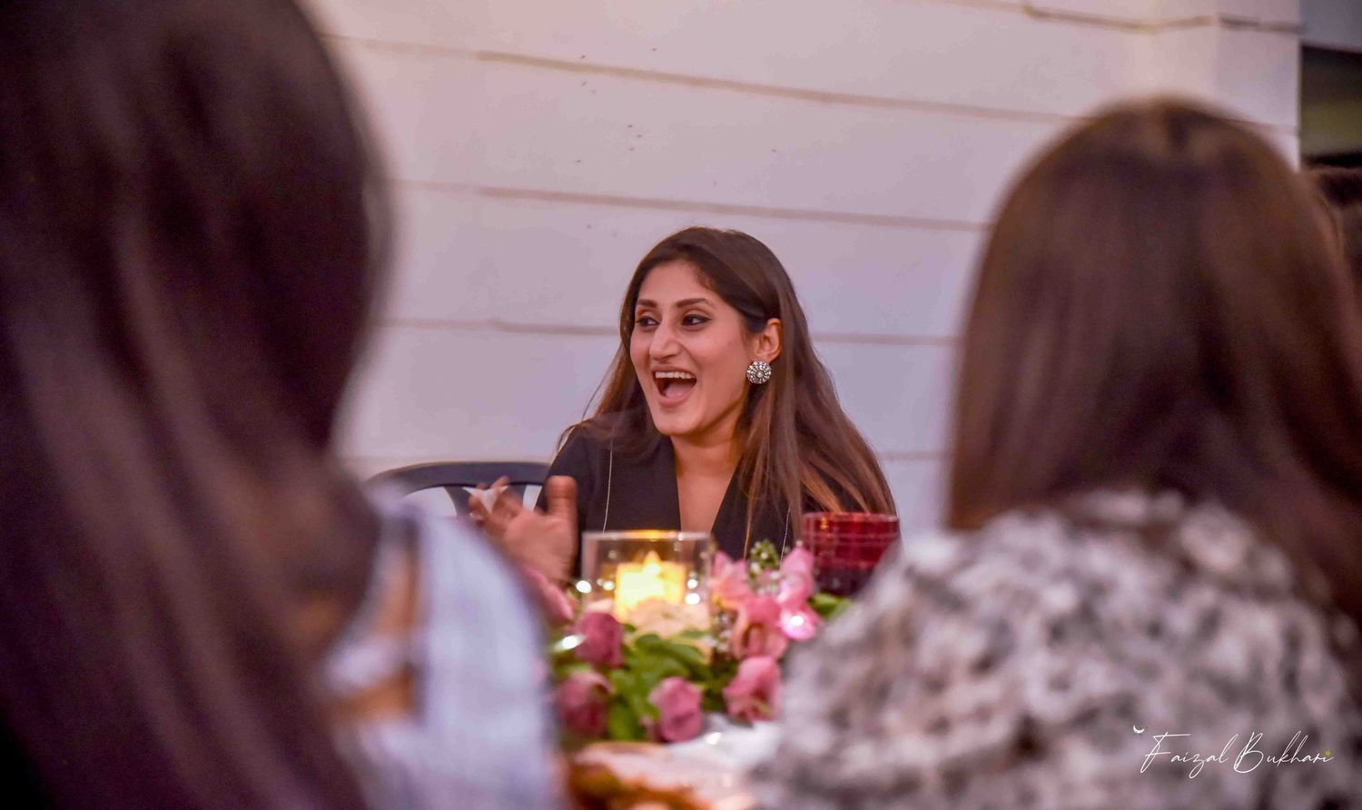 Woman laughing joyfully at candlelit outdoor bridal shower dinner table with floral centerpiece.