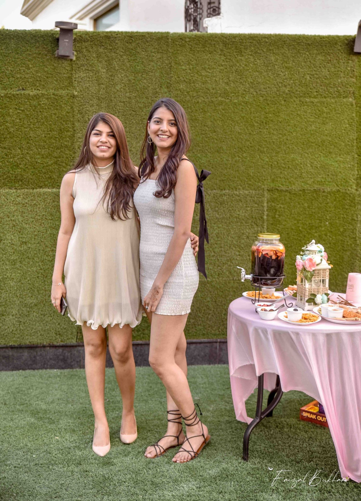 Two women posing together at an outdoor bridal shower party with dessert table.