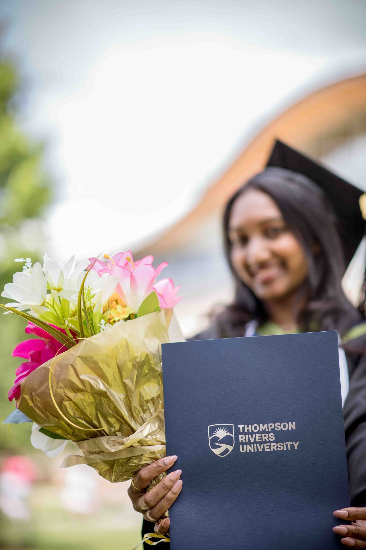 Thompson Rivers University graduate holds diploma and bouquet of colorful flowers at convocation.