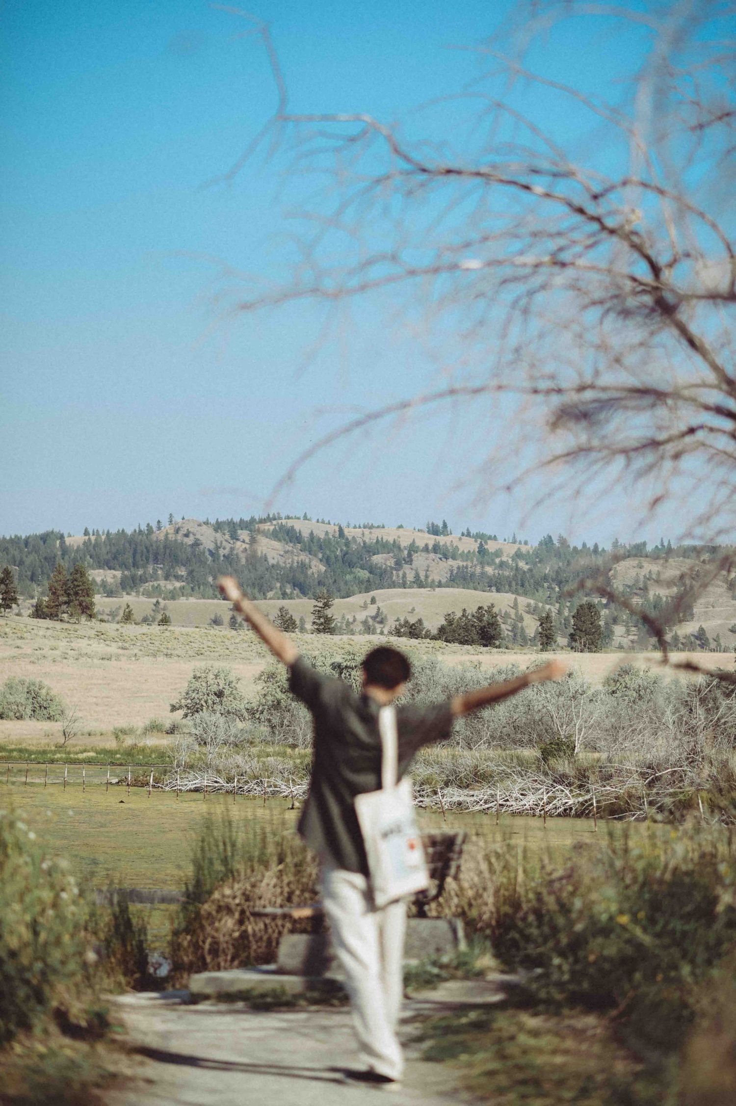 Kamloops student with a tote bag cheering by a pond. Scenic mountain backdrop. Professional lifestyle portraiture in the BC Interior & Loops