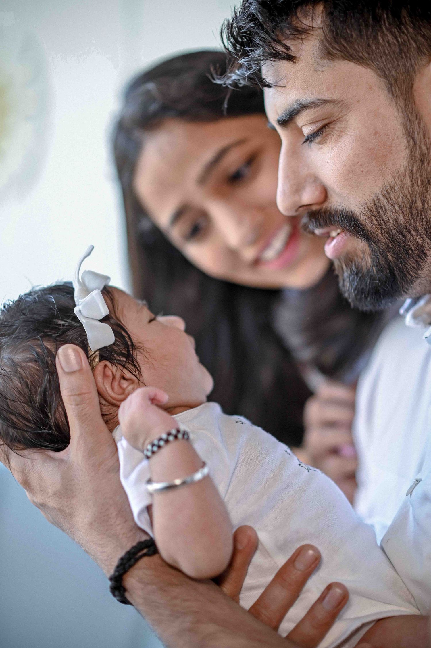 A couple tenderly gazes at their newborn baby girl wearing a white bow headband.