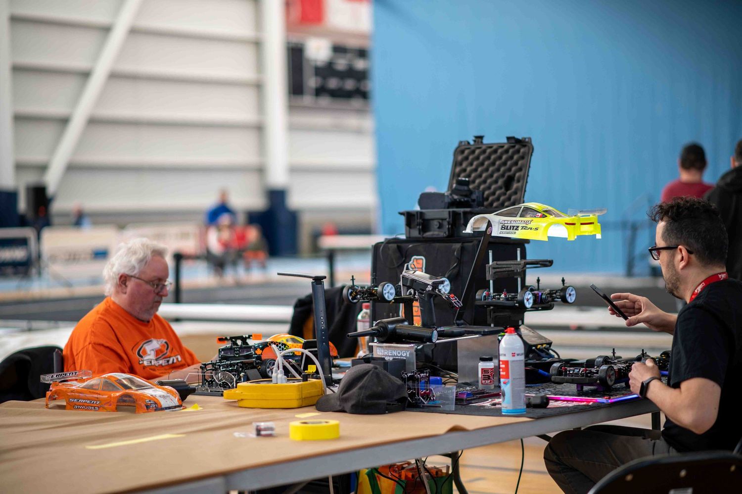 Hobbyists working on RC cars and equipment at indoor racing event.
