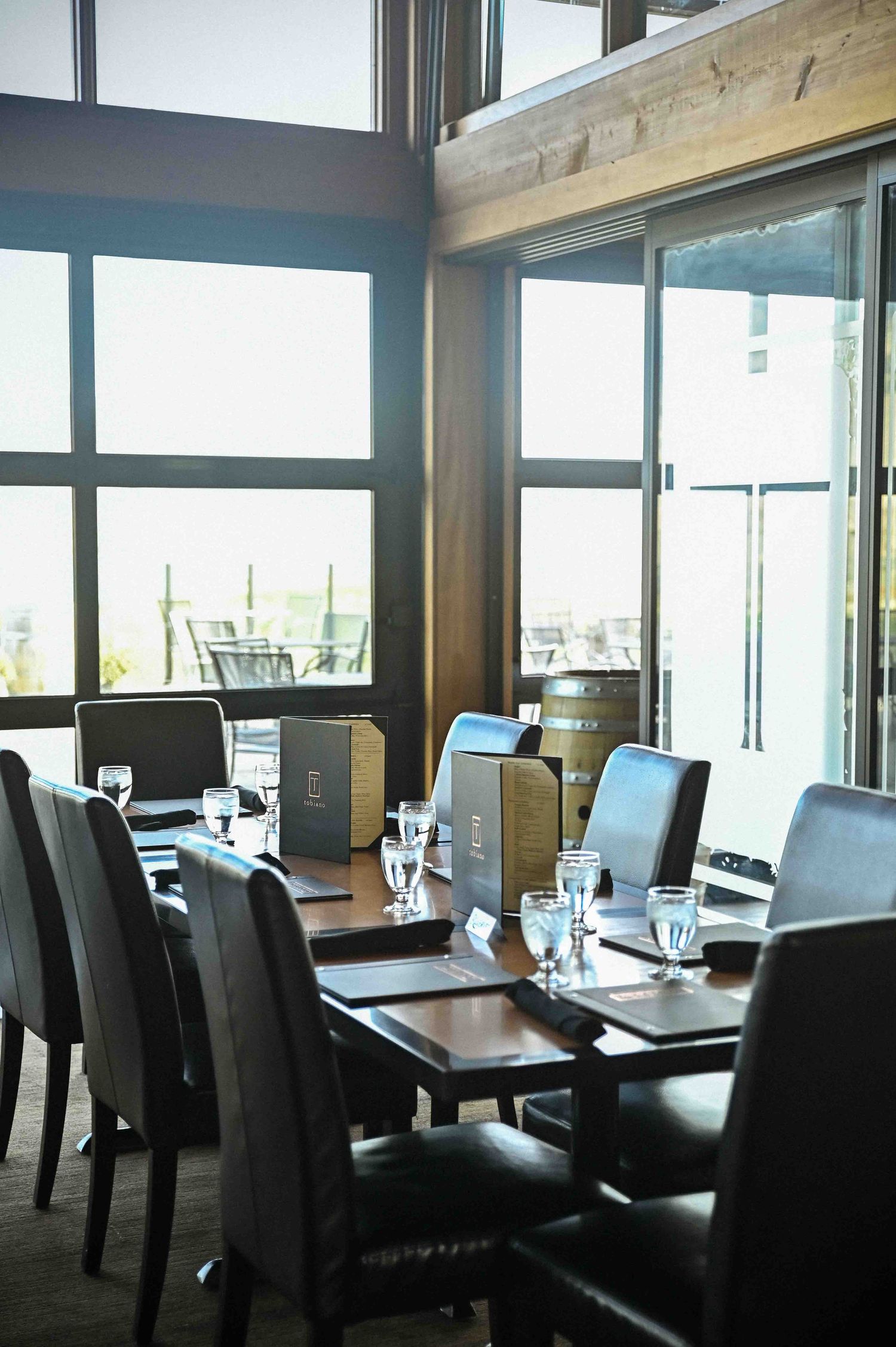 Elegant restaurant dining room with large windows, leather chairs, and neatly set tables.