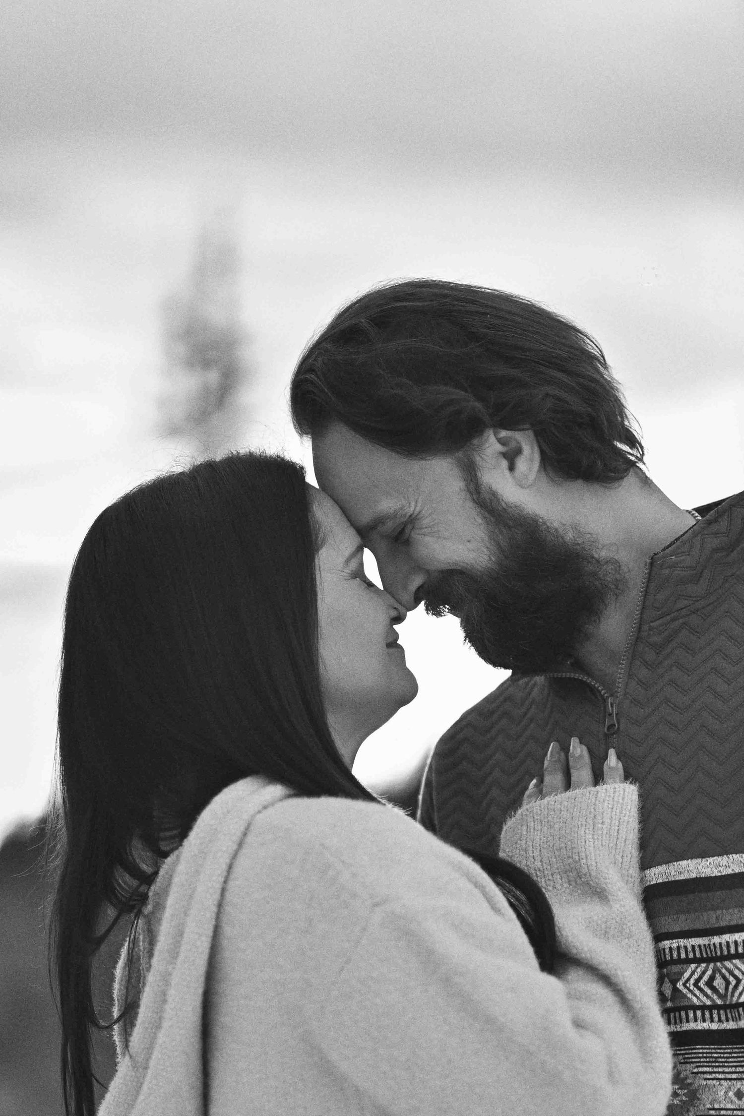 Black and white romantic close-up of couple sharing a tender kiss outdoors during winter engagement shoot.