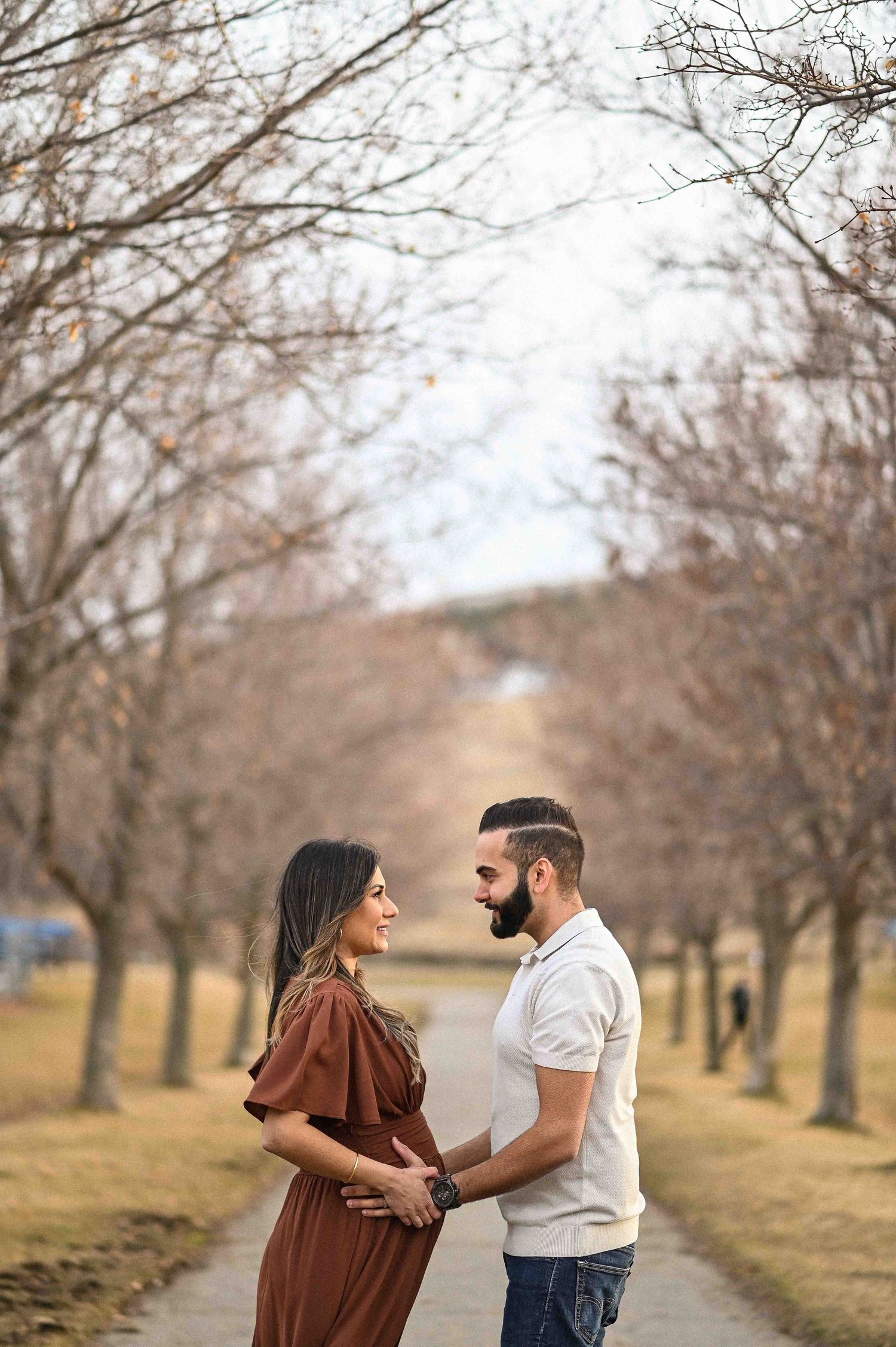 Couple sharing a tender maternity moment on a tree-lined path in autumn.