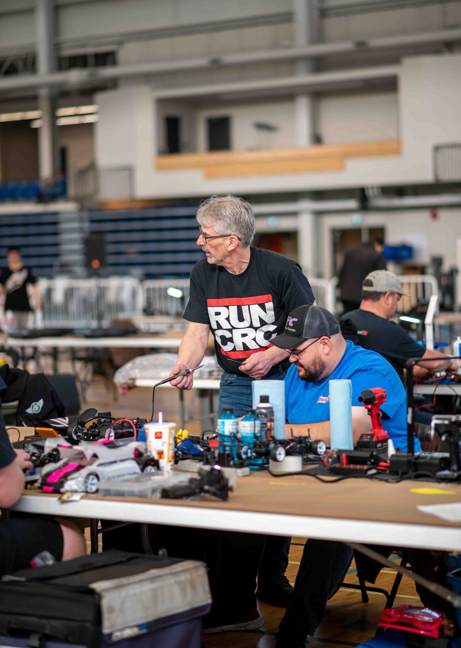 Men working on RC cars at table during indoor radio-controlled racing event.
