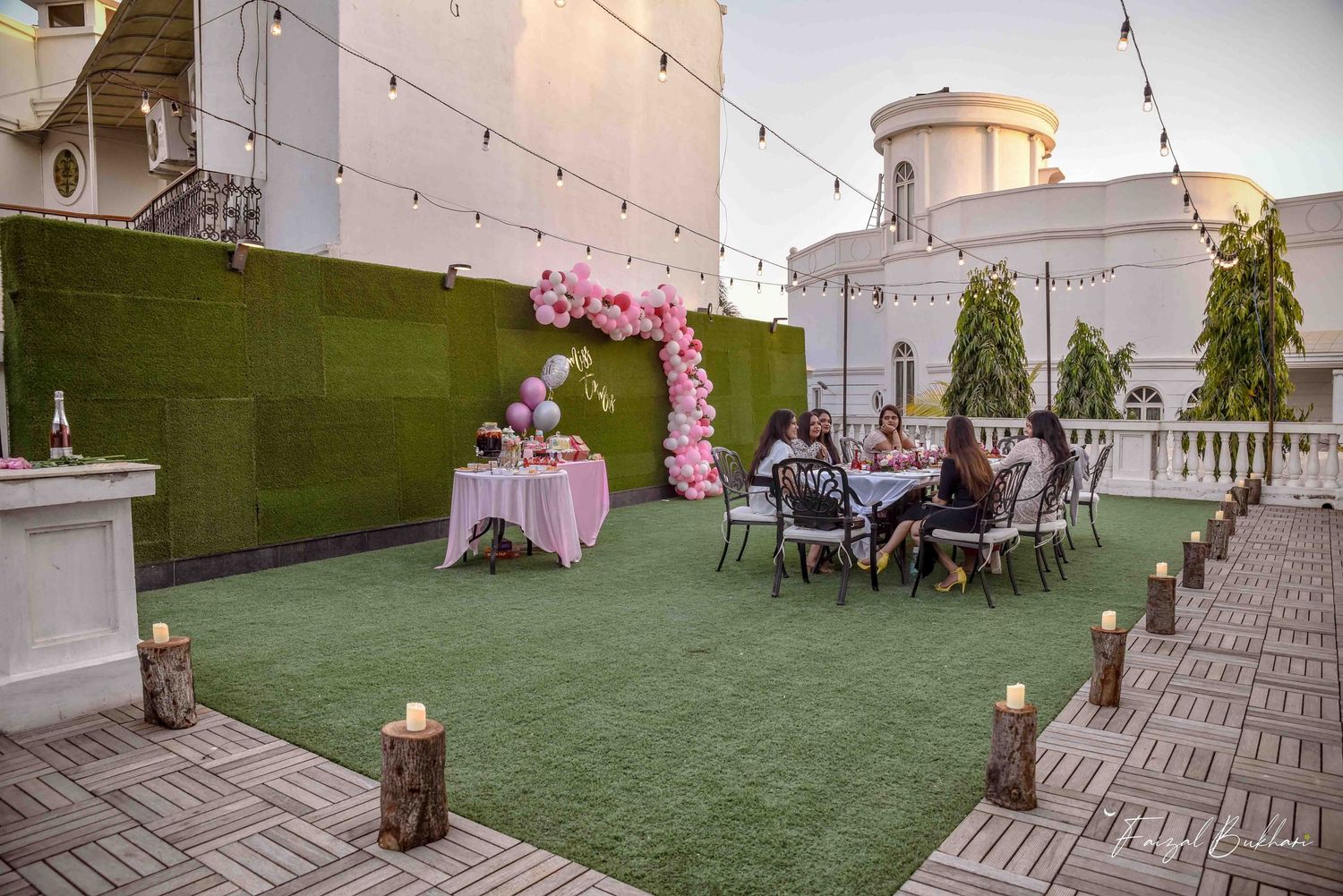 Rooftop bridal shower setup with pink balloon arch, candles, and string lights at dusk.