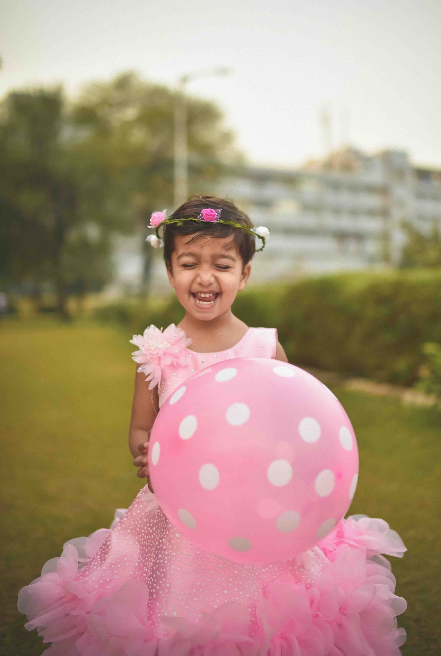 Joyful young girl in pink tutu dress holding polka dot balloon with floral crown outdoors.