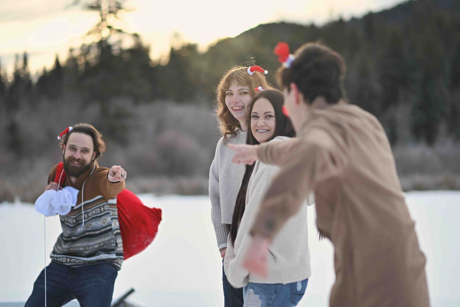 Group of four family members laughing and playing outdoors near a frozen lake during a festive winter photo session.