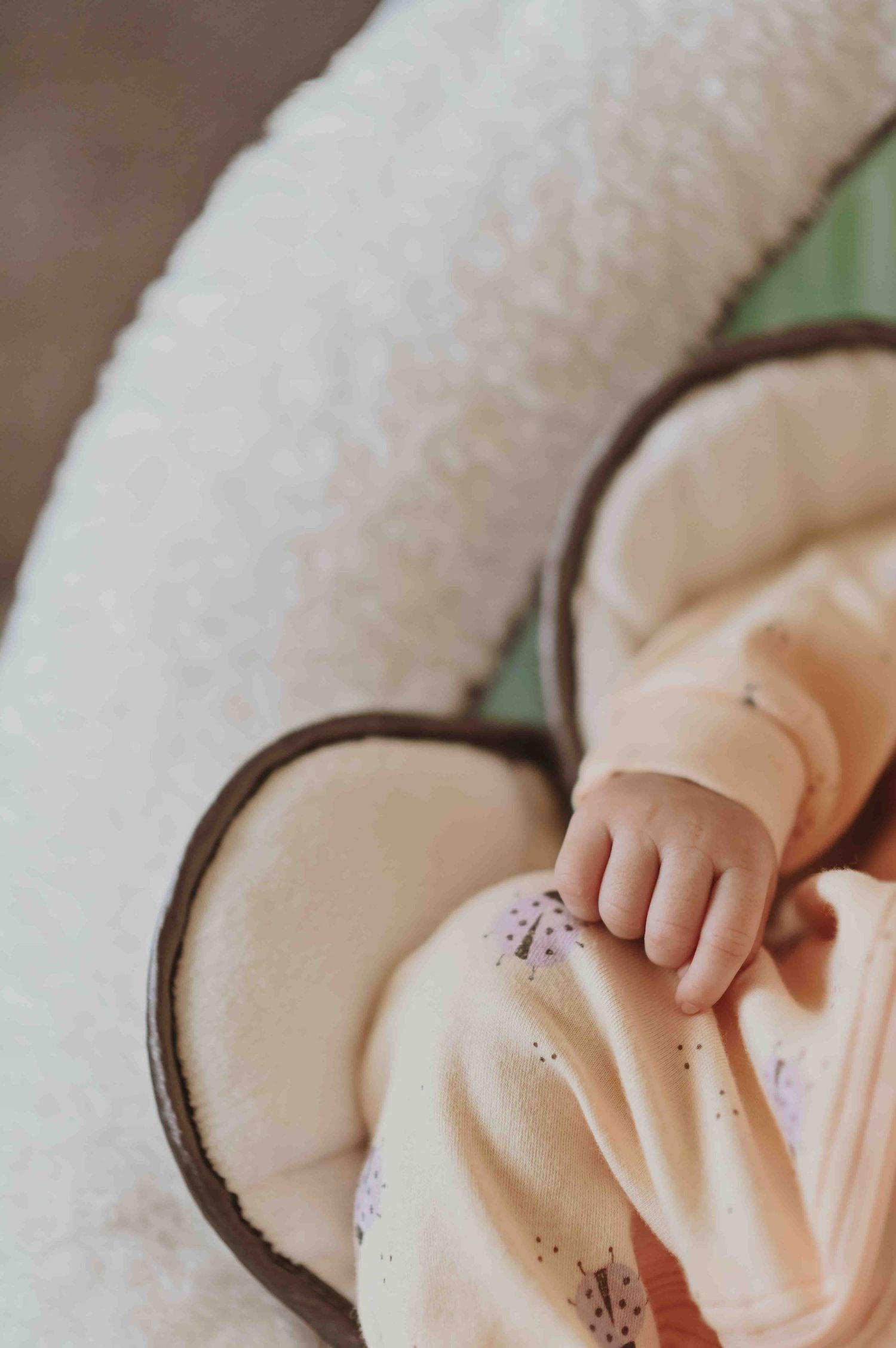 Newborn baby sleeps peacefully in a cozy cream-colored baby lounger seat.