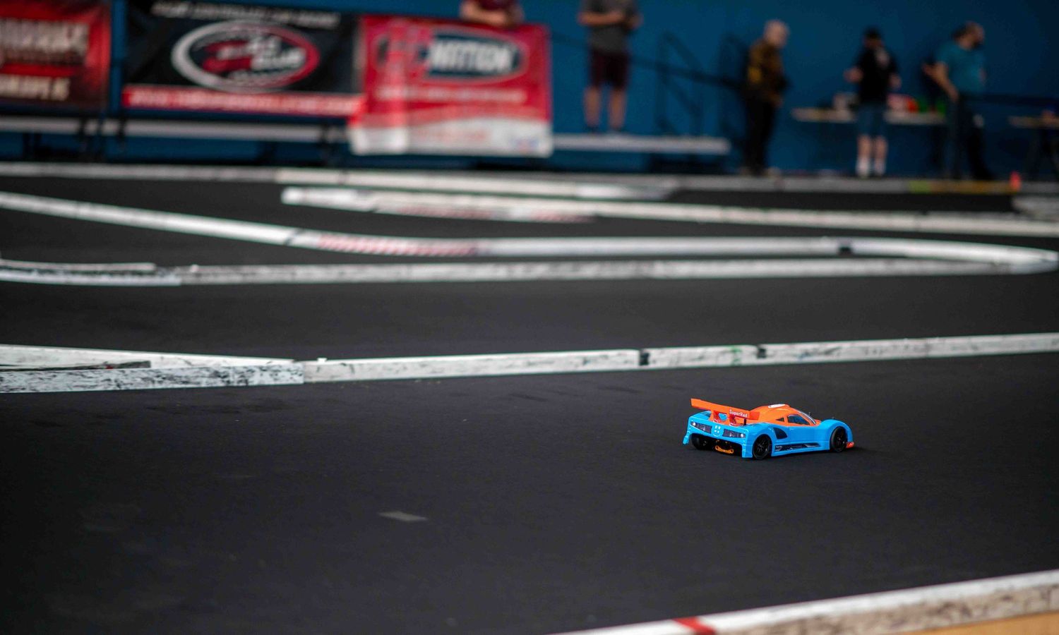 Blue and orange RC touring car speeding along a smooth indoor racing track.