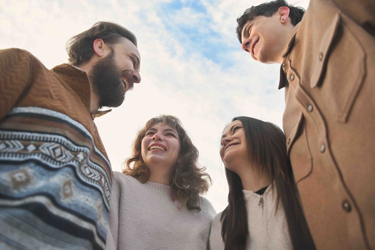 Four friends smiling and laughing together in a close huddle during an outdoor winter photo session.