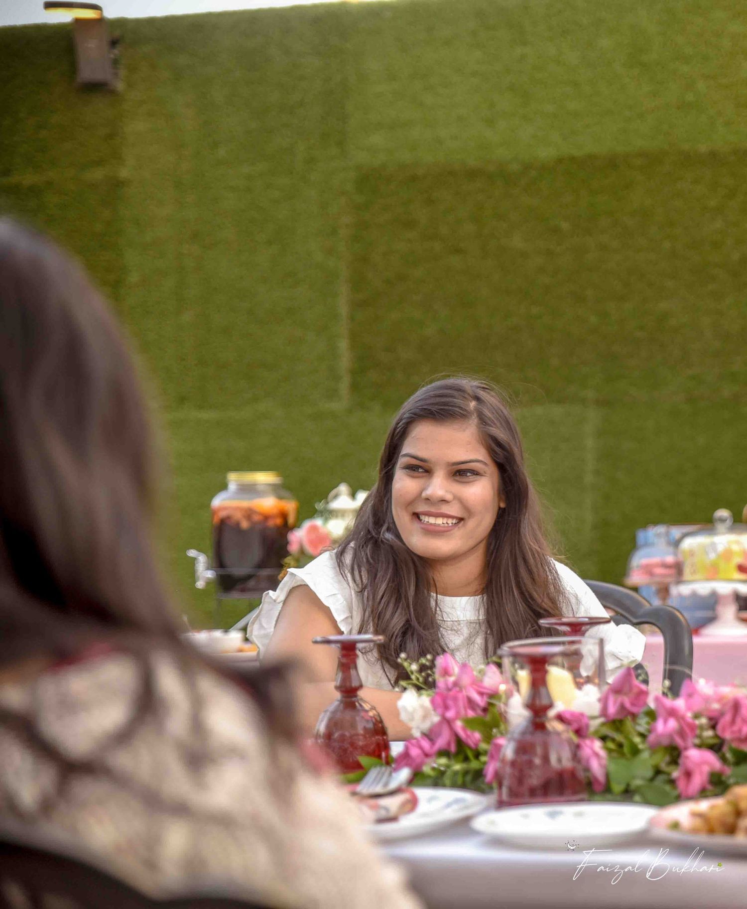 Smiling woman at outdoor bridal shower table with pink flowers and festive decorations.