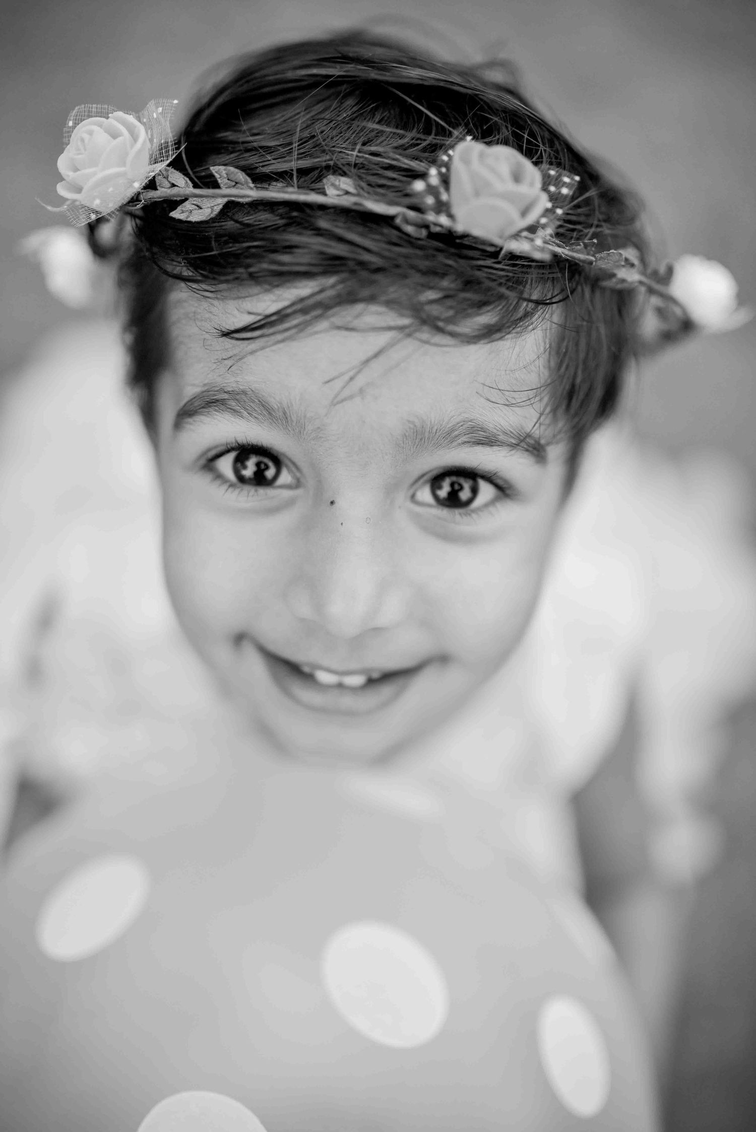 Black and white close-up portrait of a cute girl wearing a floral crown looking up.