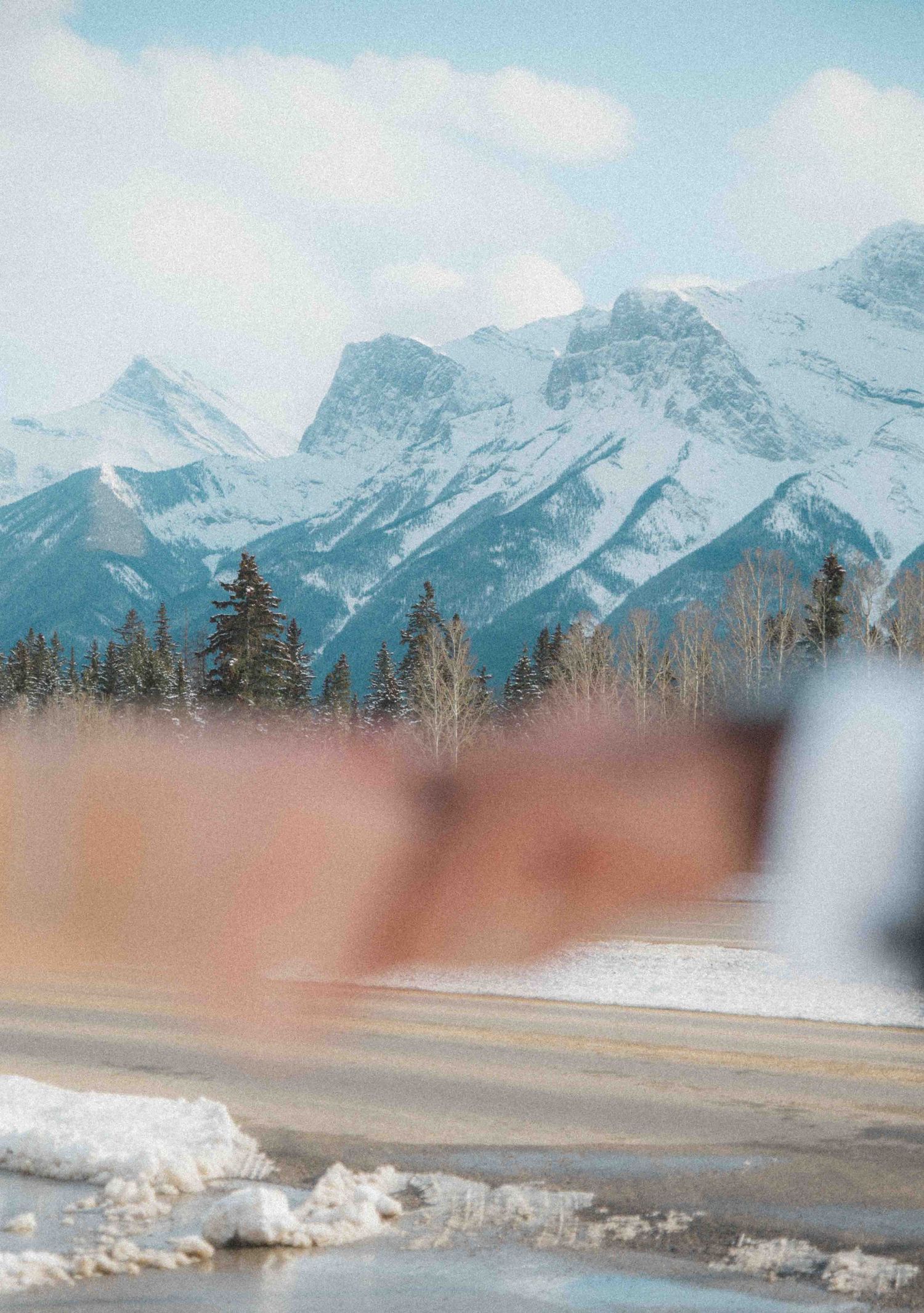 Snow-capped Rocky Mountains with evergreen trees visible through car window on scenic winter wedding day drive.