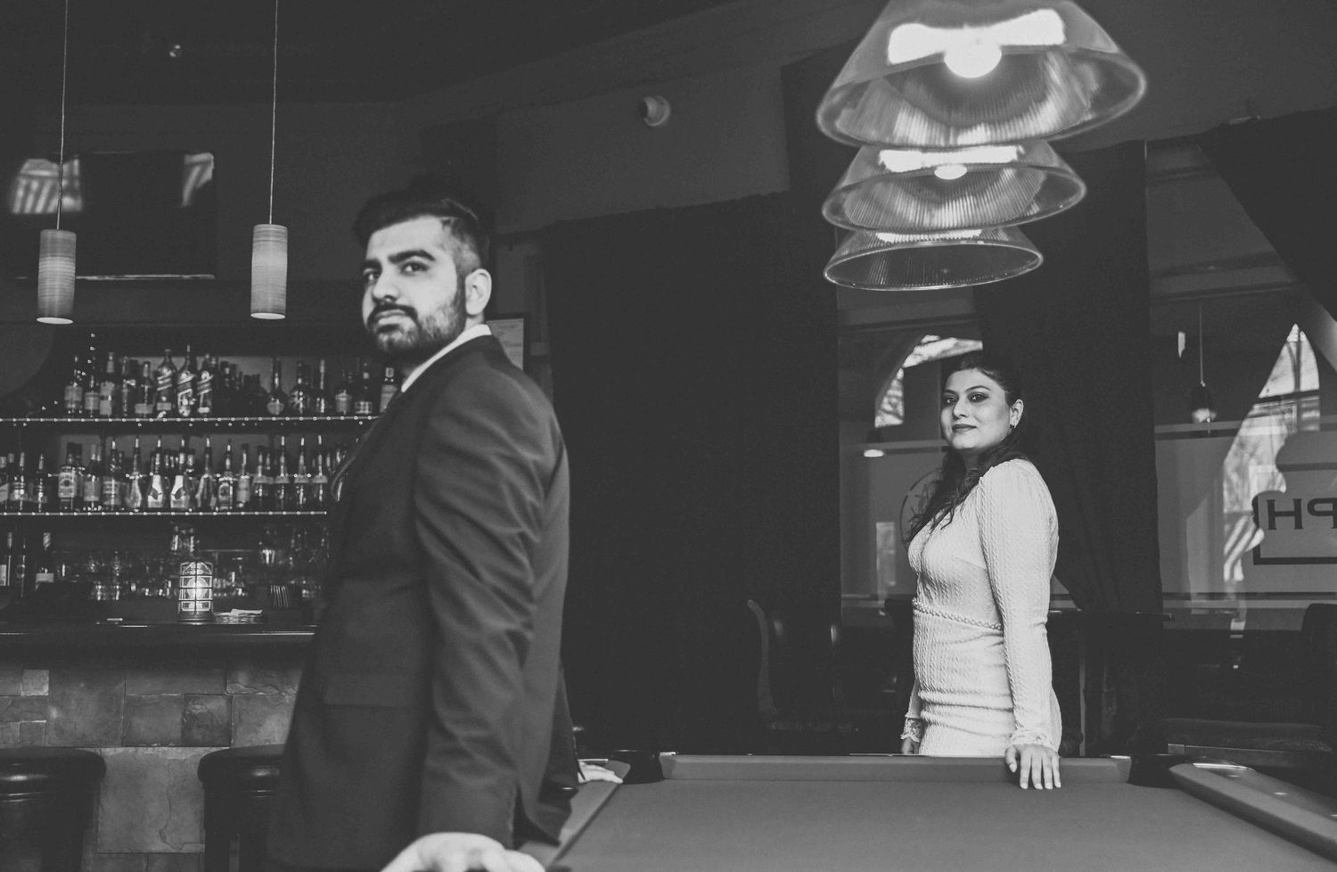 Stylish couple posing near a pool table in a bar, black and white photo.