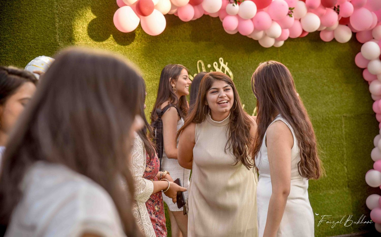 Women celebrating at a bridal shower with pink balloon arch backdrop.