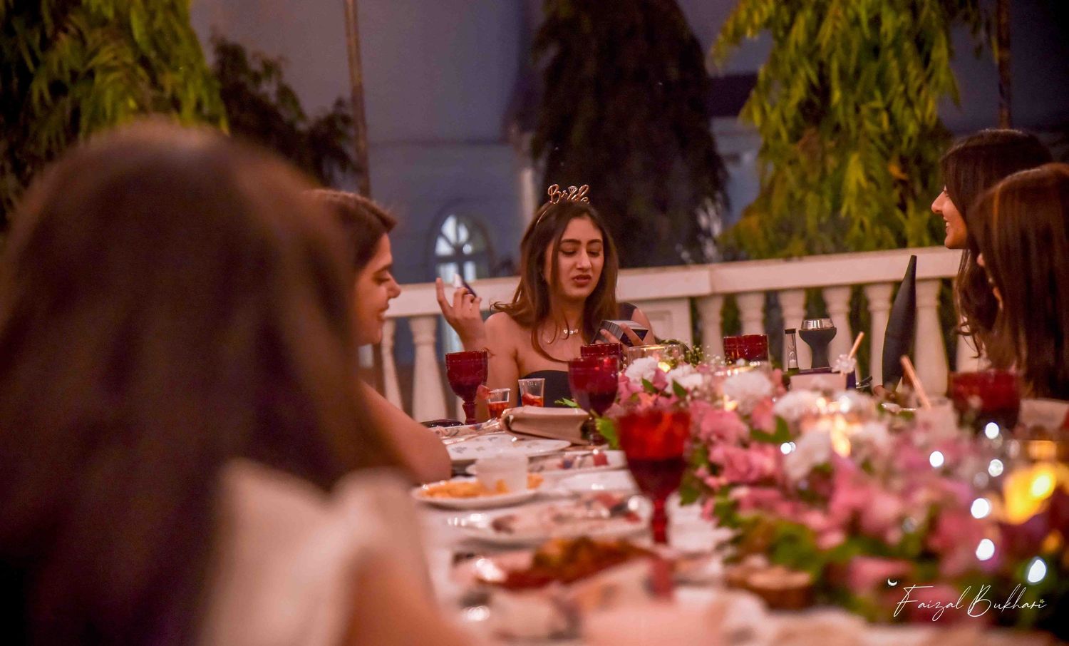 Woman in crown at candlelit dinner party table with red goblets.