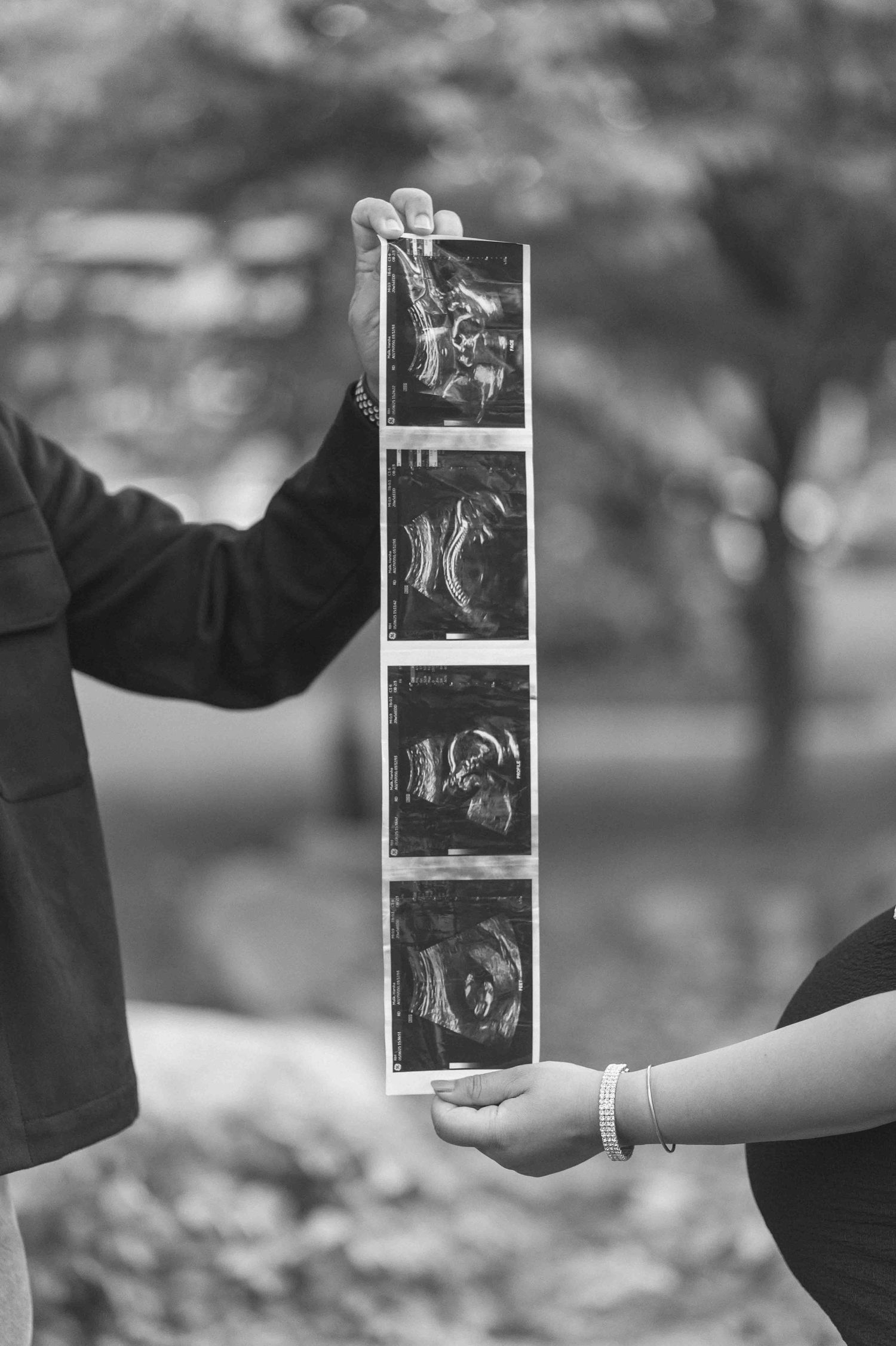 Couple holding ultrasound photos outdoors in black and white maternity announcement photo.