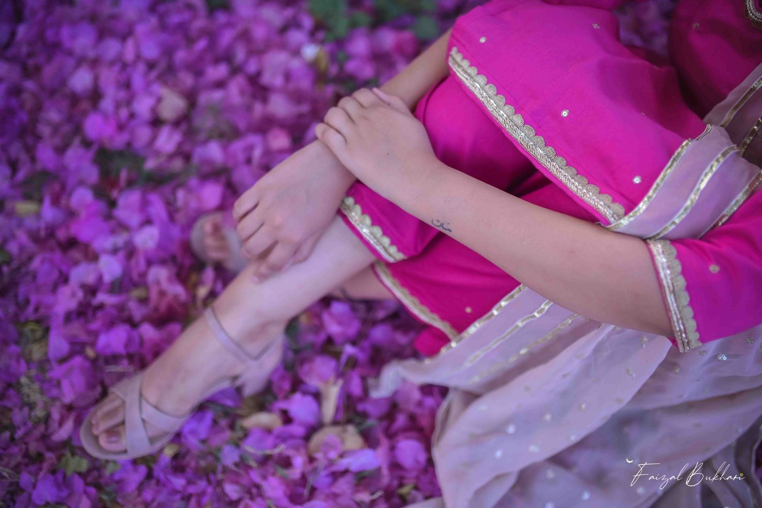 A woman in a pink and gold traditional Indian outfit sits among scattered purple flower petals.
