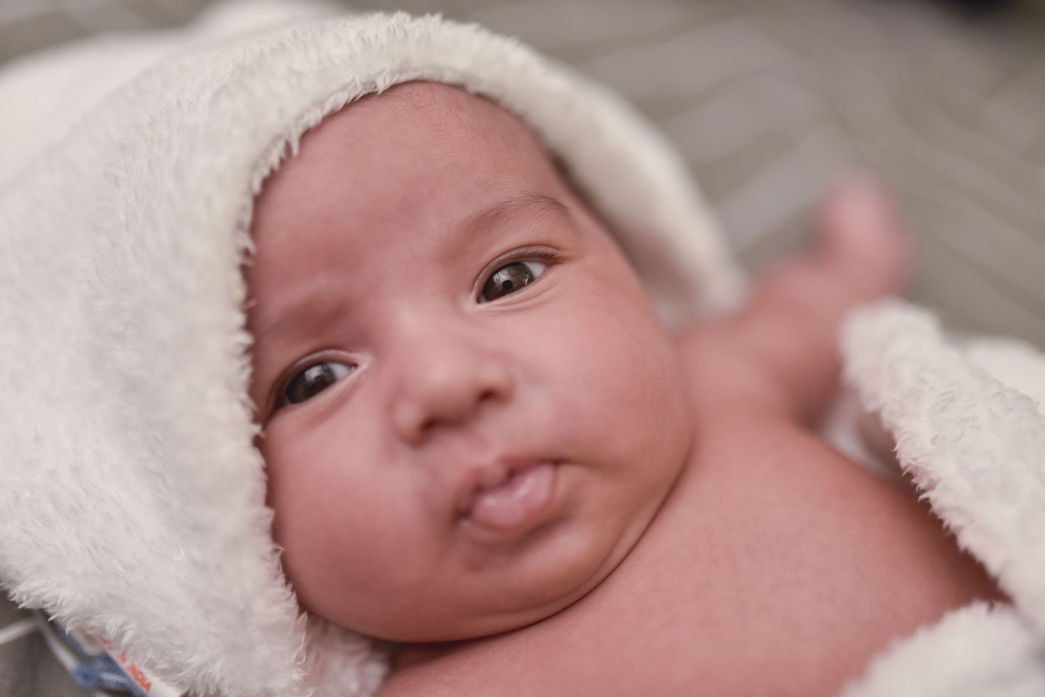 Adorable newborn baby wrapped in a white hooded towel with alert dark eyes.