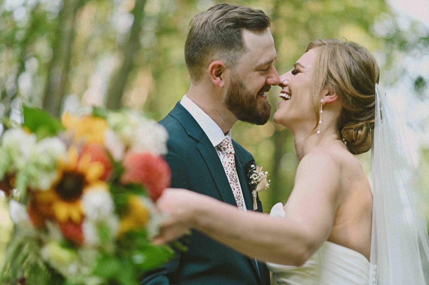 A smiling bride and groom share a tender moment surrounded by vibrant sunflower wedding bouquets.