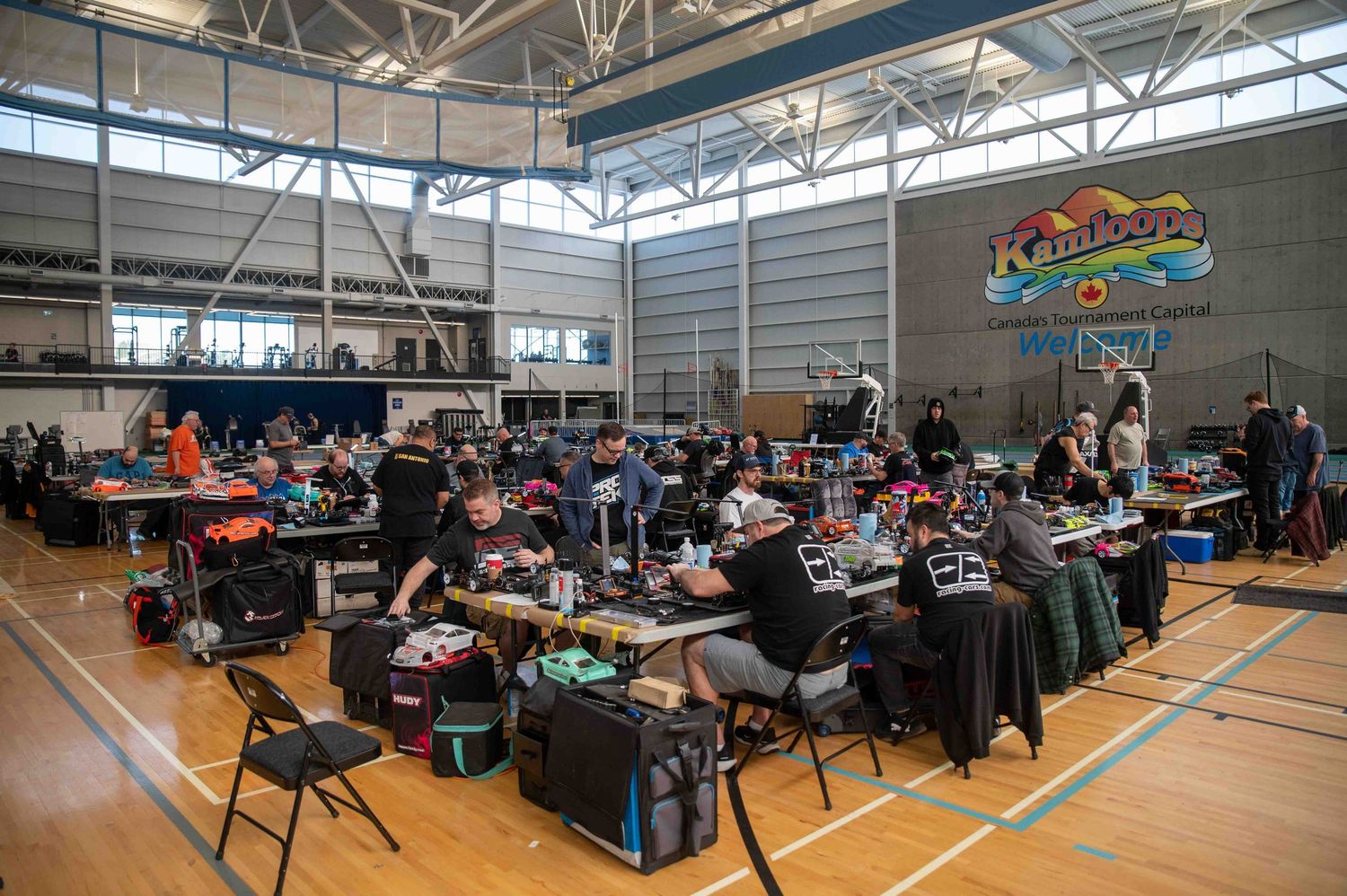 Large indoor RC car racing event with participants gathered in gymnasium.
