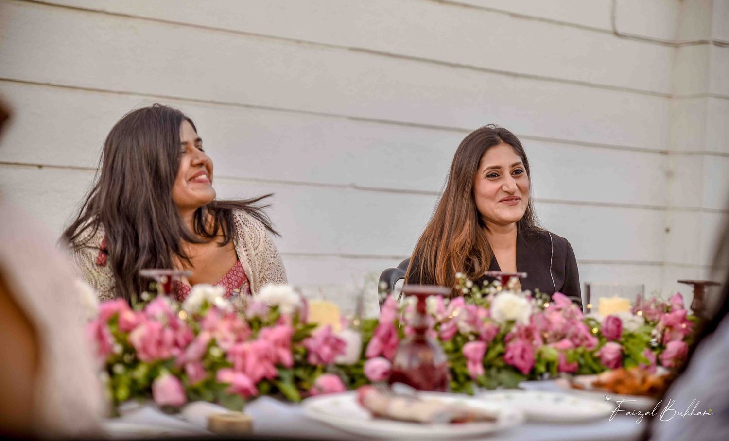 Two women laughing together at floral-decorated outdoor bridal shower table.