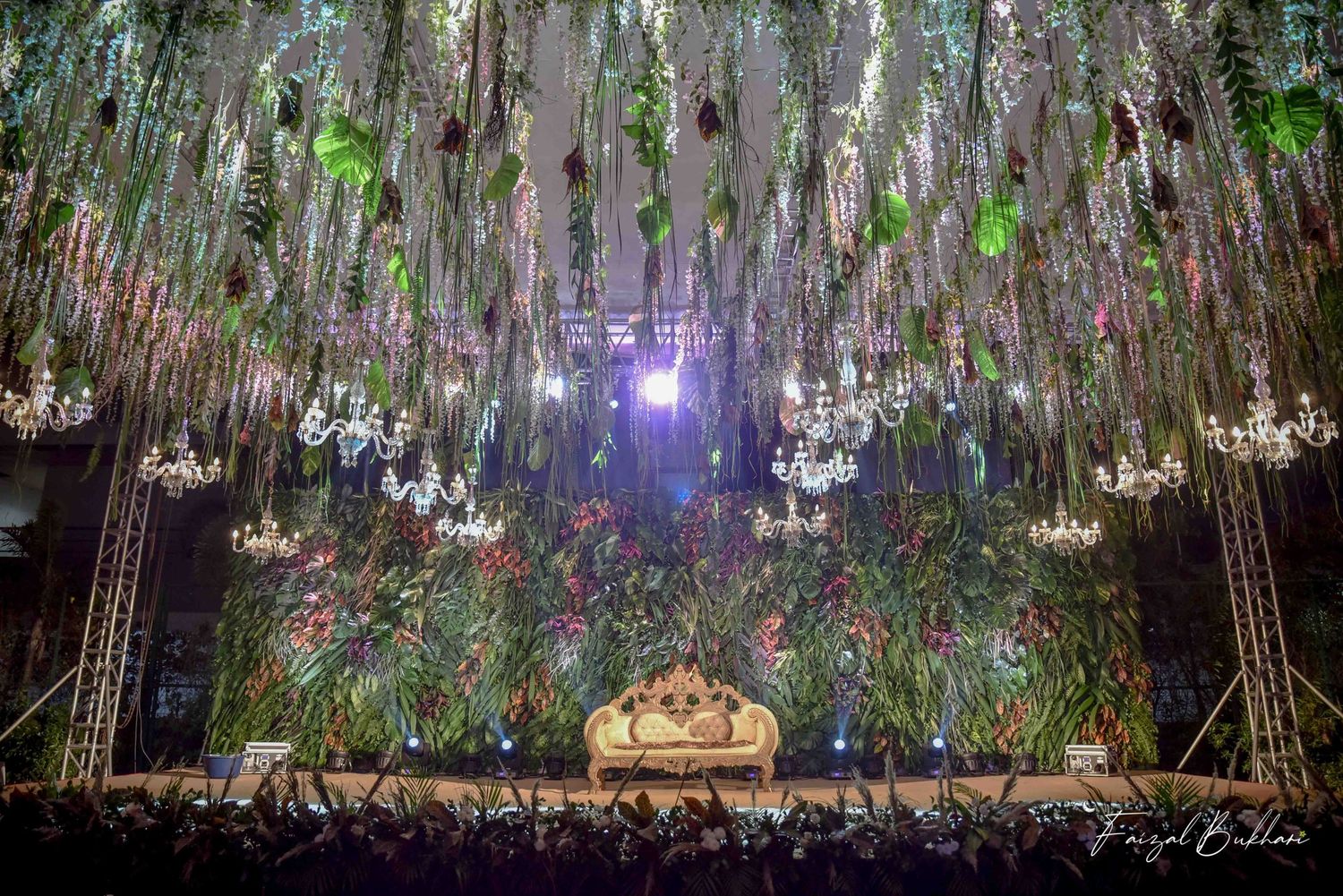 Stunning wedding venue decorated with hanging chandeliers, lush greenery, and floral ceiling installation.