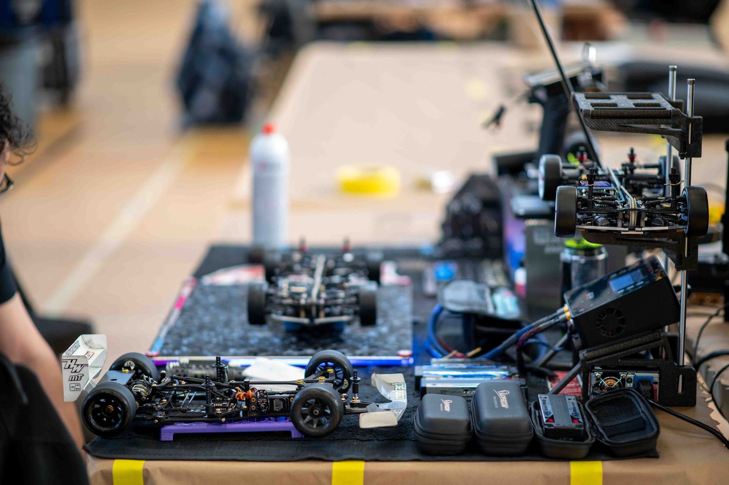 RC car chassis and components laid out on a workbench at an indoor RC racing event.