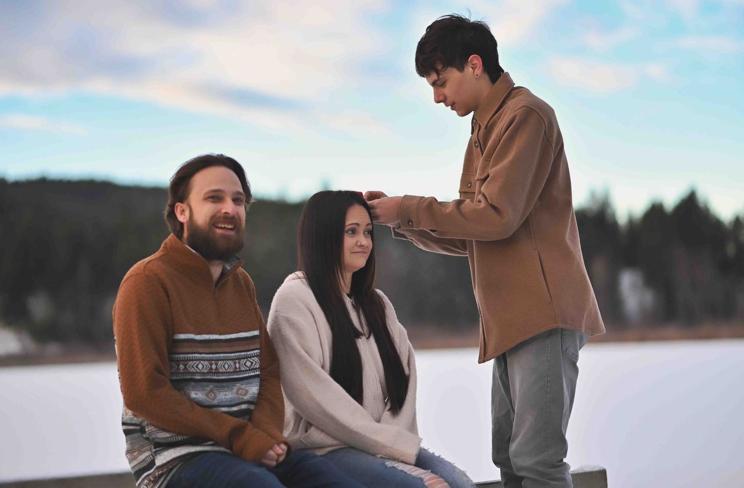 Young man adjusts woman's hair while bearded man watches during a winter outdoor photo session.