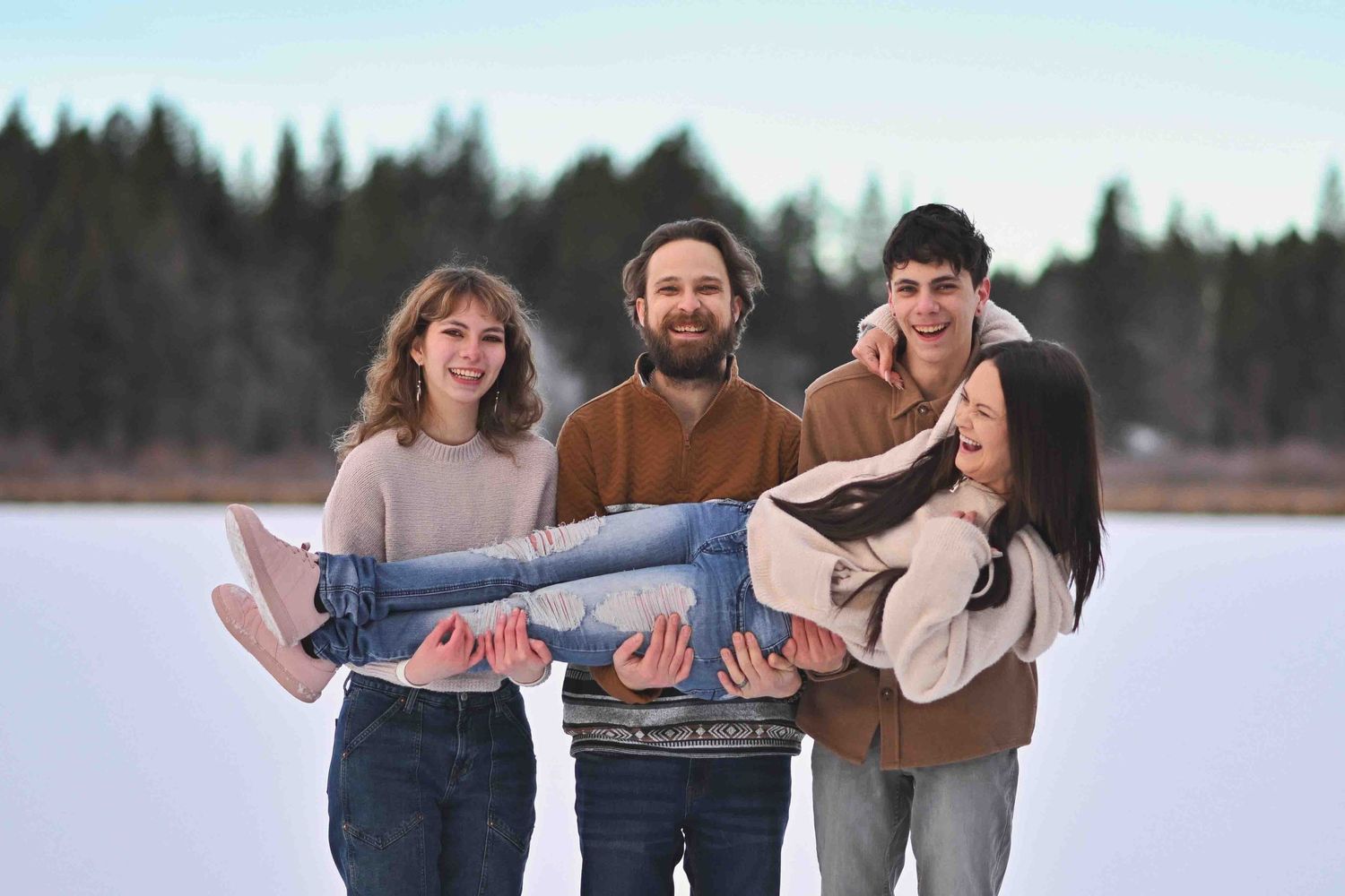 Joyful family of four posing playfully on a frozen lake with pine forest backdrop in winter.