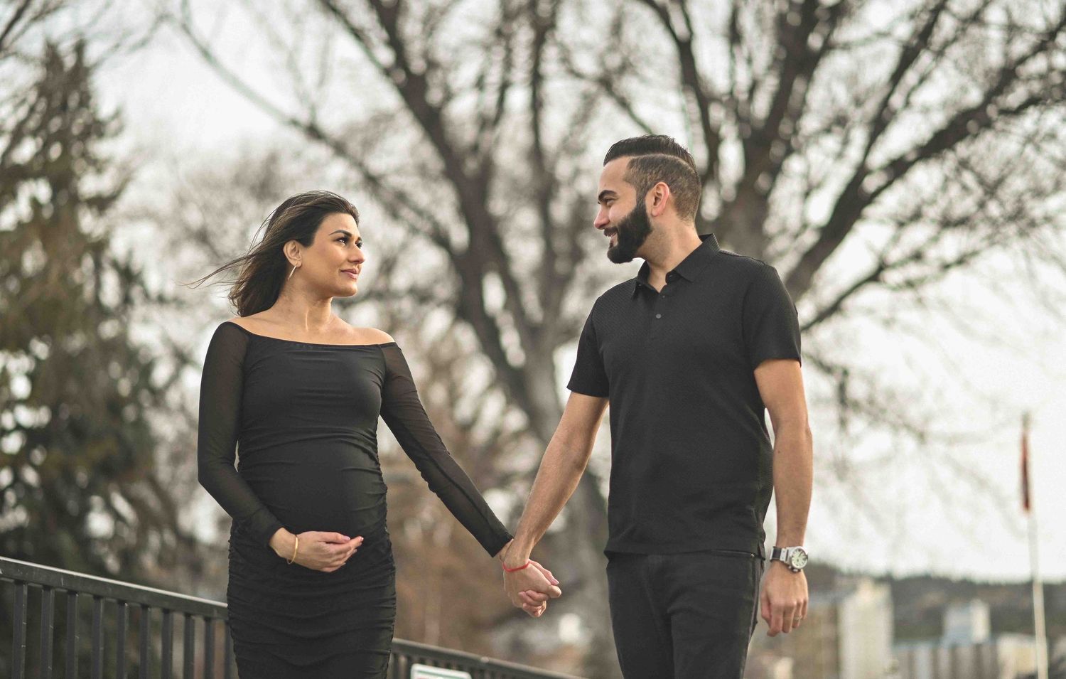 Smiling expecting couple holding hands near a railing during outdoor maternity shoot.